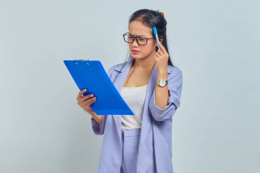 Kafasını kalemle kaşıyan, fikirleri düşünen ve mor arka planda izole edilmiş bir pano tutan Asyalı genç iş kadınının portresi.