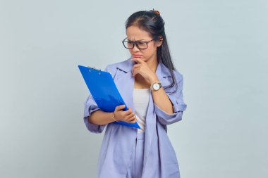 Ciddi bir Asyalı iş kadınının portresi. Çenesini tutuyor, elinde mor arka planda izole edilmiş belge klasörünü tutarken bir şeyler düşünüyor.