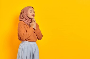 Sarı arka planda, gözleri kapalı dua eden güzel Asyalı genç bir kadının portresi. İnsanlar İslam dini kavramları