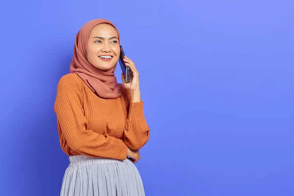 紫の背景の上に隔離されながら 携帯電話で話す茶色のセーターとヒジャーブで美しいアジアの女性を笑顔 人々は宗教的概念を — ストック写真