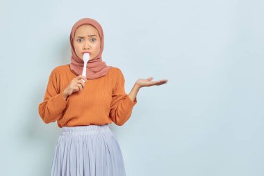 Kahverengi kazaklı, tesettürlü ve tesettürlü güzel Asyalı kadın beyaz arka planda izole edilmiş ellerde kopya alanı gösteriyor.