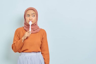 Ağzında kaşık tutan kahverengi kazaklı, aç, güzel Asyalı kadın beyaz arka planda izole edilmiş lezzetli yemekleri düşün.