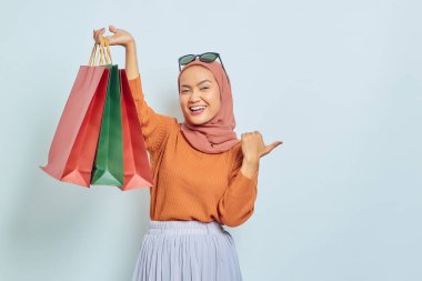 Kahverengi kazaklı ve gözlüklü güzel Asyalı Müslüman kadın fotokopi alanını işaret ederken beyaz arka planda izole edilmiş parmaklarını gösteriyor. Dünya Tüketici Hakları Günü Kavramı