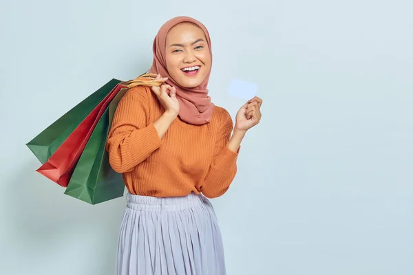 戴着太阳镜 棕色毛衣 头戴头巾 头戴信用卡的快乐美丽的亚洲穆斯林女性 在白色背景下购物后拿着购物袋购物 — 图库照片