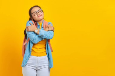 Sırt çantasıyla sırtüstü sırtüstü uzanmış gülümseyen Asyalı genç bayan öğrenci sarı arka planda kendini soyutlanmış hissediyor. Üniversite konsepti eğitimi