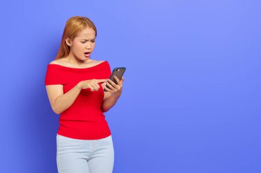 Kırmızı elbiseli genç Asyalı bir kadının portresi mesaj yazarken ya da sosyal ağda mor arkaplan üzerinde izole akıllı telefon kullanarak kaydırırken.