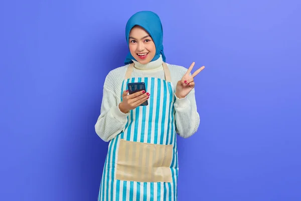 대젊은 아시아 앞치마를 핸드폰을 보라색 배경에 손가락 고립된 표시를 사람들 — 스톡 사진