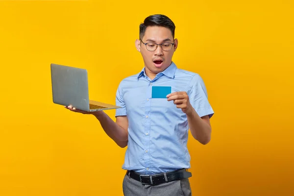 令人惊讶的是 亚洲年轻人戴着眼镜 手里拿着笔记本电脑 看上去像一个被黄色背景隔离的信用卡 商人和企业家概念 — 图库照片