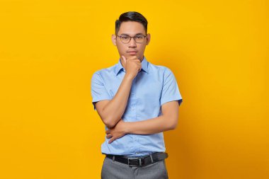 Gözlüklü düşünceli genç Asyalı adamın portresi sarı arka planda izole edilmiş bir çenenin altında el ele tutuyor. İş adamı ve girişimci konsepti