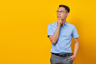Gözlüklü düşünceli genç Asyalı adamın portresi sarı arka planda izole edilmiş bir çenenin altında el ele tutuyor. İş adamı ve girişimci konsepti