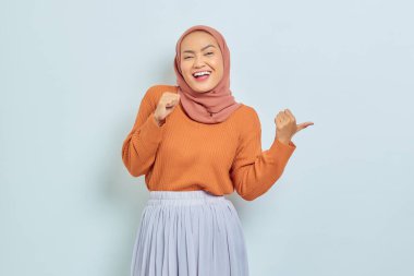 Kahverengi kazaklı, tesettürlü, tesettürlü, tesettürlü, reklam ürünlerini gösteren ve beyaz arka planda izole edilmiş kameraya bakan güzel bir Asyalı kadın..