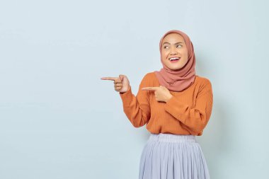Kahverengi kazaklı, tesettürlü, tesettürlü, tesettürlü, reklam ürünlerini gösteren ve beyaz arka planda izole edilmiş kameraya bakan güzel bir Asyalı kadın..