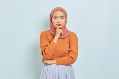 Kahverengi kazaklı, Asya 'lı genç bir Müslüman kadının portresi, çenesini tutuyor ve ciddi bir şekilde düşünüyor soru soruyor ve beyaz arka planda izole edilmiş kameraya bakıyor. Müslüman yaşam tarzı kavramı