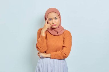 Kahverengi kazaklı güzel bir Asyalı genç Müslüman kadının portresi. Soruyu ciddi ciddi düşünüyor ve beyaz arka planda izole edilmiş kameraya bakıyor. Müslüman yaşam tarzı kavramı