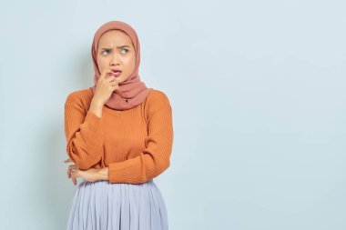 Kahverengi kazaklı, Asyalı genç ve güzel bir kadının portresi soru sormayı ve beyaz arka planda izole edilmiş parmağını ısırmayı ciddi ciddi düşünüyor. Müslüman yaşam tarzı kavramı