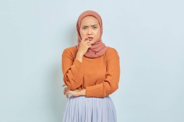 Kahverengi kazaklı, Asyalı genç ve güzel bir kadının portresi soru sormayı ve beyaz arka planda izole edilmiş parmağını ısırmayı ciddi ciddi düşünüyor. Müslüman yaşam tarzı kavramı