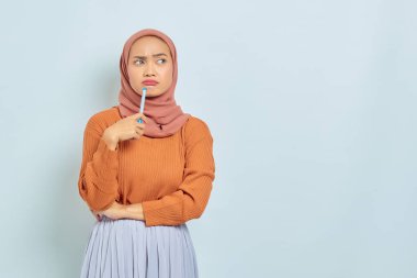 Kahverengi kazaklı ve tesettürlü güzel Asyalı kadın beyaz arka planda izole edilmiş bir soru hakkında ciddi düşünüyor. Müslüman yaşam tarzı kavramı