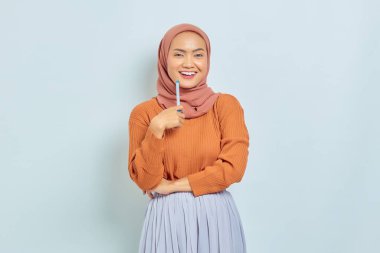 Kahverengi kazaklı, tesettürlü, tesettürlü güzel Asyalı kadın beyaz arka planda izole edilmiş bir soru hakkında ciddi düşünüyor. Müslüman yaşam tarzı kavramı