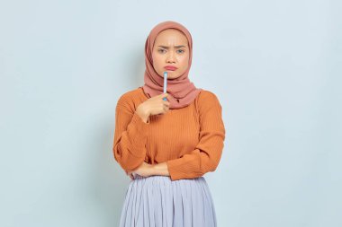 Kahverengi kazaklı ve tesettürlü güzel Asyalı kadın beyaz arka planda izole edilmiş bir soru hakkında ciddi düşünüyor. Müslüman yaşam tarzı kavramı