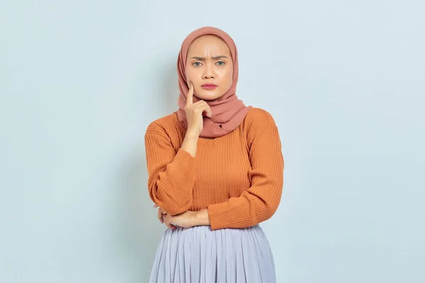茶色のセーターを着た美しい若いアジア系イスラム教徒の女性の肖像画と質問について真剣に考え 白い背景に孤立したカメラを見ています イスラム教徒のライフスタイルコンセプト — ストック写真