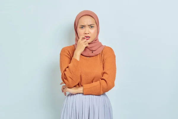 茶色のセーターを着た美しい若いアジア系イスラム教徒の女性の肖像画は 白い背景に隔離された質問とかむ指について真剣に考えています イスラム教徒のライフスタイルコンセプト — ストック写真