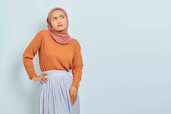 茶色のセーターを着た美しい若いアジア系ムスリム女性の肖像画は 混乱した顔の表情で立っており 白い背景に孤立したコピースペースを見ています イスラム教徒のライフスタイルコンセプト — ストック写真