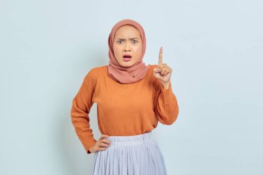 Kahverengi kazaklı Asyalı genç Müslüman kadın beyaz arka planda parmak izolasyonuyla fotokopi alanını işaret ediyor. Müslüman yaşam tarzı kavramı