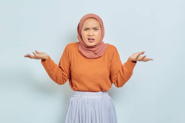 Kafası karışmış, kahverengi kazaklı, avuçları beyaz arka planda olan ve hayır diyen Asyalı Müslüman bir kadının portresi. Müslüman yaşam tarzı kavramı