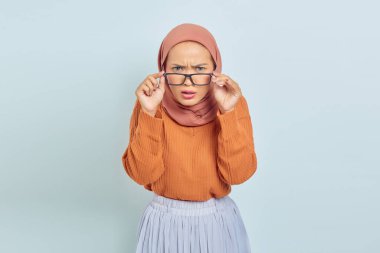 Kafası karışmış, kahverengi kazaklı ve beyaz arka planda izole edilmiş kameraya bakan genç bir Asyalı Müslüman kadının portresi. Müslüman yaşam tarzı kavramı