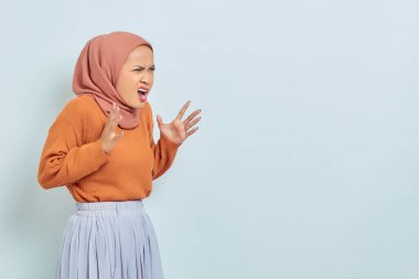 Kızgın genç Asyalı kadın portresi histerik bir şekilde çığlık atıyor ve beyaz arka planda izole bir şekilde yan bakıyor.