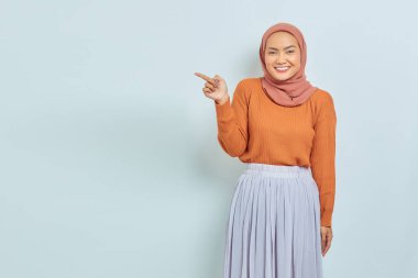 Kahverengi kazaklı, tesettürlü, tesettürlü, tesettürlü, reklam ürünlerini gösteren ve beyaz arka planda izole edilmiş kameraya bakan güzel bir Asyalı kadın..