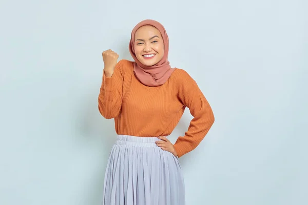 茶色のセーターを着た興奮した若いアジア系イスラム教徒の女性は 白の背景に隔離されたはいと言って拳を祝う勝利のジェスチャーをしています イスラム教徒のライフスタイルコンセプト — ストック写真