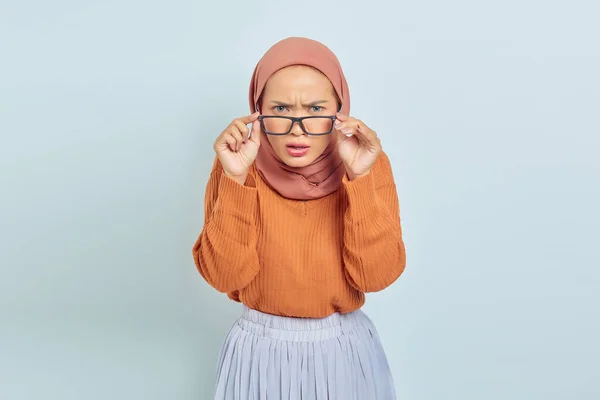 眼鏡をかけ 白い背景に隔離されたカメラを見ている茶色のセーターの混乱した若いアジア系イスラム教徒の女性の肖像画 イスラム教徒のライフスタイルコンセプト — ストック写真