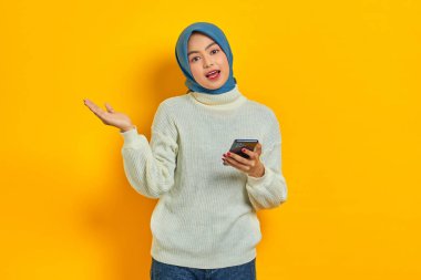 Sarı arka planda izole edilmiş beyaz kazaklı ve tesettürlü neşeli Asyalı kadın portresi. İnsanlar İslam dini kavramları