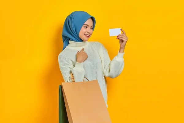 身穿白色毛衣 头戴黄色背景的购物袋和信用卡的快乐美丽的亚洲女人 — 图库照片