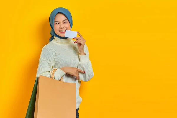 朗らかな若いアジアの女性かむクレジットカードとホールドショッピングバッグ上の黄色の背景 — ストック写真