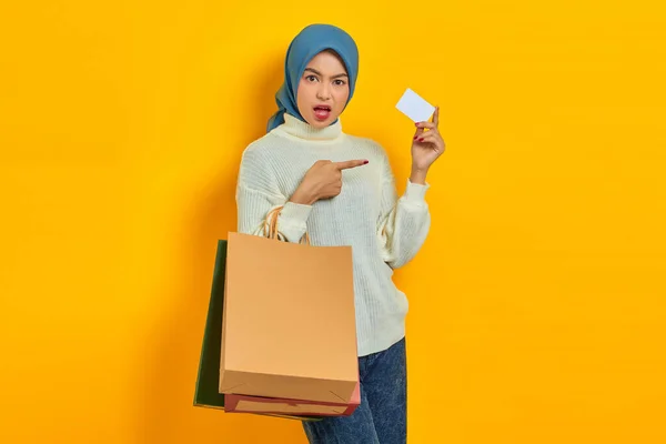 漂亮的亚洲女人 身穿白色毛衣 手握购物袋 用手指指指黄底的信用卡 吓得面无血色 — 图库照片