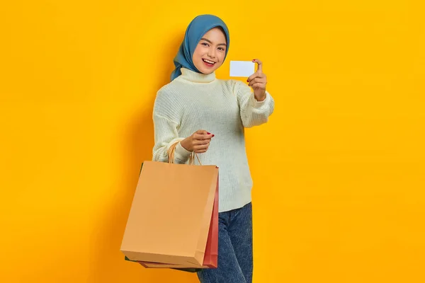 陽気美しいですアジアの女性でホワイトセーター保持ショッピングバッグとショークレジットカード絶縁上の黄色の背景 — ストック写真