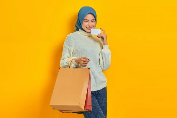 身穿白色毛衣 提着购物袋 在黄色背景下展示信用卡的快乐美丽的亚洲女人 — 图库照片