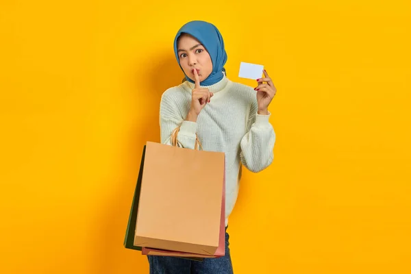 漂亮的亚洲女人 穿着白色毛衣 拿着购物袋和信用卡 在黄色的背景上做着沉默的手势 — 图库照片