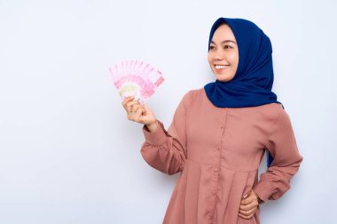 Pembe gömlekli gülümseyen Asyalı Müslüman kadın elinde para banknotları ve beyaz arka planda izole edilmiş fotokopi odasına bakıyor. İnsanlar dini yaşam tarzı konsepti