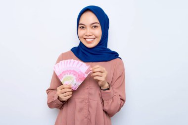 Pembe gömlekli gülümseyen Asyalı müslüman kadın elinde beyaz arka planda izole edilmiş para banknotları tutuyor. İnsanlar dini yaşam tarzı konsepti