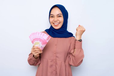 Heyecanlı pembe gömlekli, Asyalı genç Müslüman kadın beyaz arka planda izole edilmiş para banknotları tutuyor. İnsanlar dini yaşam tarzı konsepti