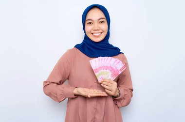 Pembe gömlekli gülümseyen Asyalı müslüman kadın elinde beyaz arka planda izole edilmiş para banknotları tutuyor. İnsanlar dini yaşam tarzı konsepti