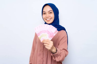 Pembe gömlekli gülümseyen Asyalı müslüman kadın elinde beyaz arka planda izole edilmiş para banknotları tutuyor. İnsanlar dini yaşam tarzı konsepti