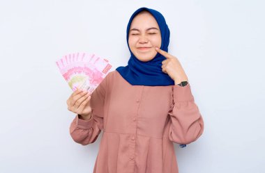 Heyecanlı pembe gömlekli, Asyalı genç Müslüman kadın beyaz arka planda izole edilmiş para banknotları tutuyor. İnsanlar dini yaşam tarzı konsepti