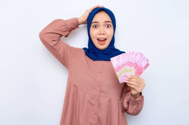 Pembe gömlekli genç Asyalı Müslüman kadın beyaz arka planda izole edilmiş para banknotları tutuyor. İnsanlar dini yaşam tarzı konsepti