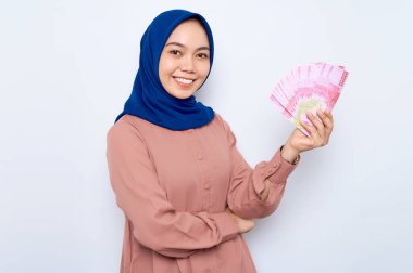 Pembe gömlekli gülümseyen Asyalı müslüman kadın elinde beyaz arka planda izole edilmiş para banknotları tutuyor. İnsanlar dini yaşam tarzı konsepti