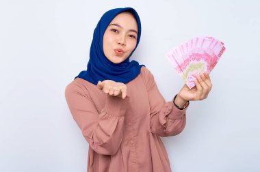 Pembe gömlekli gülümseyen Asyalı müslüman kadın elinde para banknotları ve avuç içleri tutarak beyaz arka plan üzerinden hava öpücüğü gönderiyor. İnsanlar dini yaşam tarzı konsepti