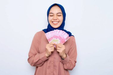 Pembe gömlekli gülümseyen Asyalı müslüman kadın elinde beyaz arka planda izole edilmiş para banknotları tutuyor. İnsanlar dini yaşam tarzı konsepti